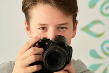 Beyaz arka planda elinde kamera olan bir çocuğun portresi.