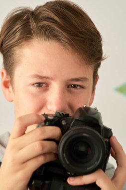 Beyaz arka planda elinde kamera olan bir çocuğun portresi.