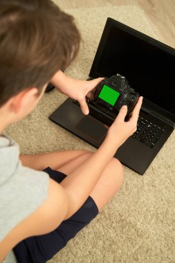 Bilgisayarın yanında kamerası olan bir çocuk monitördeki fotoğraflara bakıyor. Yeşil ekranı izle