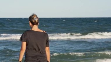Gün ışığında deniz dalgalarına bakan bir kadın.