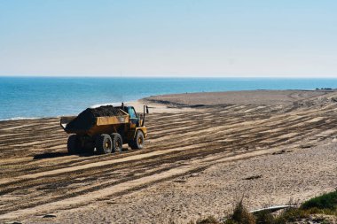 Büyük bir çöp kamyonu ıssız bir sahilde çalışıyor.