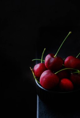 Küçük bir kase kirazda, masanın üstünde birkaç tane böğürtlen var.