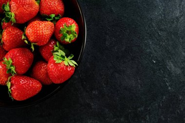 Siyah arka planda bir kase kırmızı olgun çilek yakın