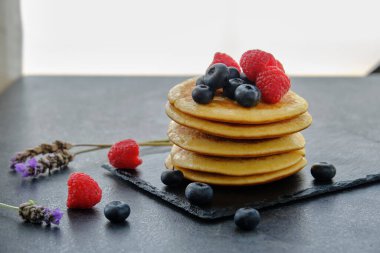 Köy kahvaltısı için taze böğürtlen ve bal kaplı bir yığın pofuduk krep.