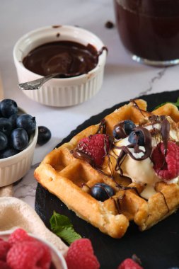 Bir tabak çikolatada Belçika waffle 'ı, ahududu, yaban mersini ve hafif bir arka planda dondurma.