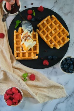 Durgun bir hayat. Siyah yuvarlak tabakta Belçika waffle 'ları. Ahududu, yabanmersini ve hafif bir arka planda dondurma.