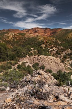 Bereketli yeşil bir vadiye bakan kayalık bir manzara ve geniş bir gökyüzü manzarası.