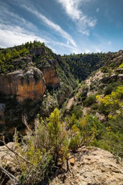 Bereketli yeşil bir vadiye bakan kayalık bir manzara ve geniş bir gökyüzü manzarası.