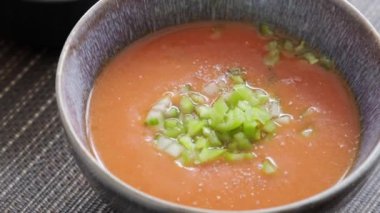 Masanın üzerinde bir tabak dolusu gazpacho ve taze sebzeler var.