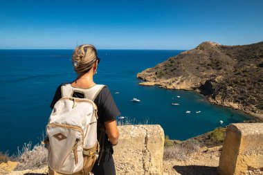 Sırt çantasıyla yüksek kıyıda duran genç bir kadın.