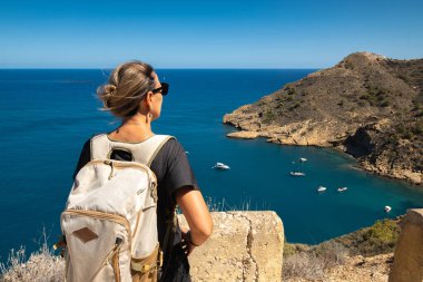 Sırt çantasıyla yüksek kıyıda duran genç bir kadın.