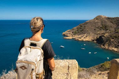 Sırt çantasıyla yüksek kıyıda duran genç bir kadın.