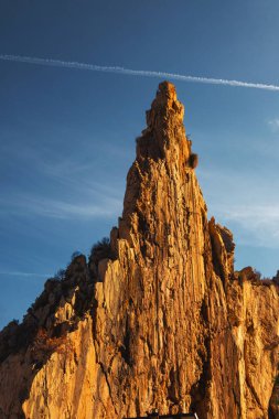 Sıcak günbatımı ışığında, mavi deniz ve gökyüzünün arka planında taş bir uçurum.