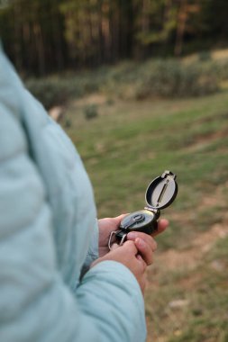 Ormanın yakınındaki bir açıklıkta bir kadın elinde bir pusula tutuyor.