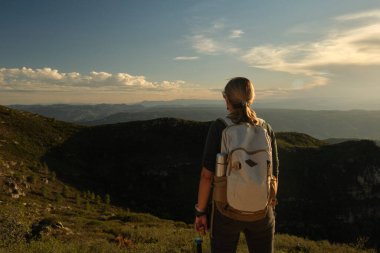 Dağın tepesinde batan güneşin altında sırt çantalı bir kadın.