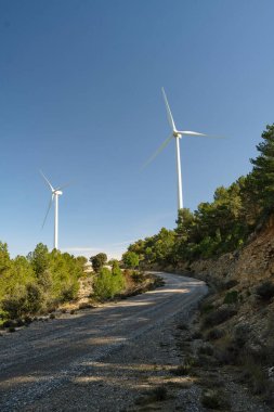 Mavi gökyüzüne karşı bir ormanın yeşiliyle çevrili bir rüzgar türbini.