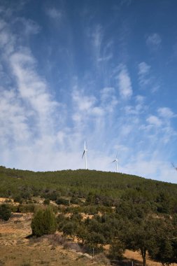 Dağların arka planında çeşitli rüzgar türbinleri var.