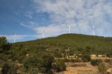 Dağların arka planında çeşitli rüzgar türbinleri var.