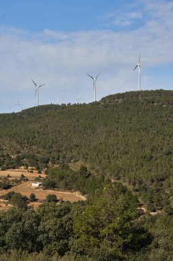 Dağların arka planında çeşitli rüzgar türbinleri var.