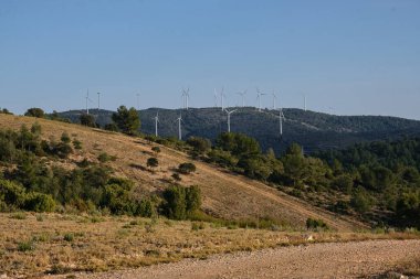 Dağların arka planında çeşitli rüzgar türbinleri var.