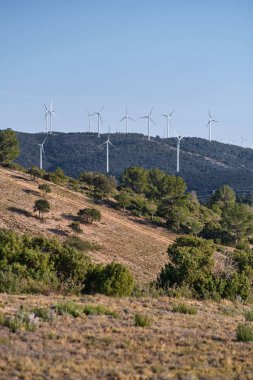 Dağların arka planında çeşitli rüzgar türbinleri var.