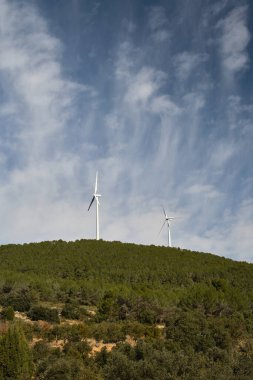 Dağların arka planında çeşitli rüzgar türbinleri var.