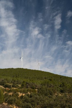 Dağların arka planında çeşitli rüzgar türbinleri var.