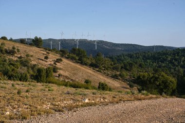 Dağların arka planında çeşitli rüzgar türbinleri var.