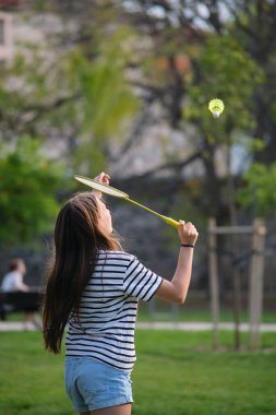 Parkta bir kız badminton oynuyor.