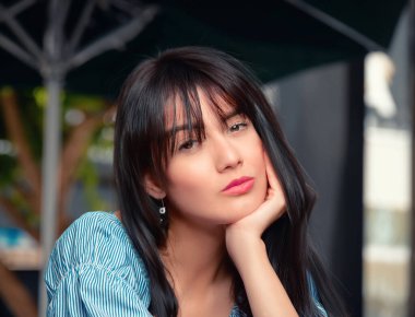 Havalı bir kahve dükkanında şık giyinmiş ve klasik siyah okuma gözlüğü takmış genç bir kadının büyüleyici fotoğrafı.