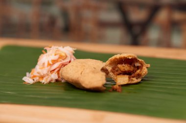 Lezzetli bir Salvador pastelito 'sunun çekici bir fotoğrafı, otantik tat ve mutfak sanatını sergiliyor, bir yaprak tarafından vurgulanmış ahşap bir yüzey üzerinde restoran tarzı bir atmosferde geçiyor.