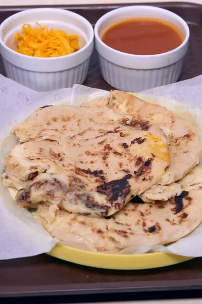 stock image Close-up photo of pupusas with curtido and sauce, served on a traditional plastic plate in a fast food tray.