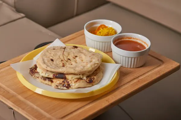 stock image Pupusas with curtido and sauce on a wooden tray, ready for movie night on a cozy theater couch