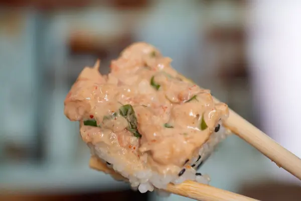 stock image Close-up of sushi held by chopsticks, with a blurred restaurant background, highlighting the fresh and vibrant cuisine.