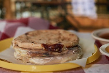 Curtido ve domates soslu Salvadorlu pupusaların yakın çekimi, canlı bir restoran ortamında servis ediliyor..
