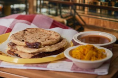Curtido ve domates soslu bir restoranda canlı bir restoranda servis edilen Salvadorlu pupusaların yakın çekimi..