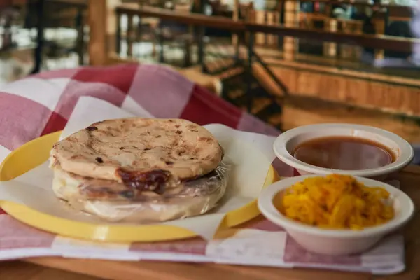 stock image Close-up of Salvadoran pupusas in a restaurant with curtido and tomato sauce, served in a vibrant restaurant setting.