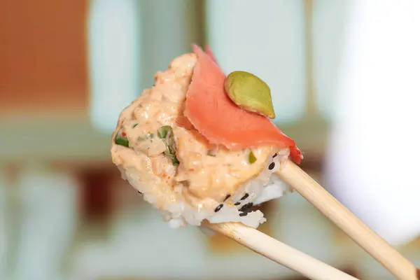 stock image Close-up of sushi with salmon and wasabi held by chopsticks, isolated against a blurred restaurant background.