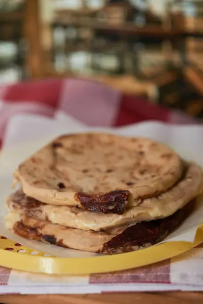 Curtido ve domates soslu Salvadorlu pupusaların yakın çekimi, canlı bir restoran ortamında servis ediliyor..