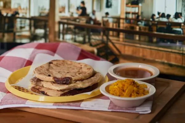 stock image Close-up of Salvadoran pupusas in a restaurant with curtido and tomato sauce, served in a vibrant restaurant setting.