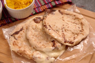 Köy ahşap bir yüzey üzerinde el yazısı ve sos ile servis edilen peynirle dolu pupusalar, canlı bir Salvador mendiliyle tamamlanmış..