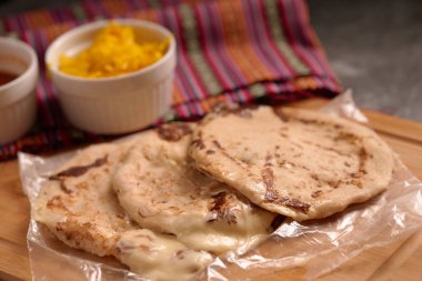 Köy ahşap bir yüzey üzerinde el yazısı ve sos ile servis edilen peynirle dolu pupusalar, canlı bir Salvador mendiliyle tamamlanmış..