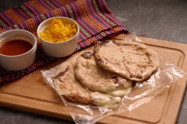 Köy ahşap bir yüzey üzerinde el yazısı ve sos ile servis edilen peynirle dolu pupusalar, canlı bir Salvador mendiliyle tamamlanmış..