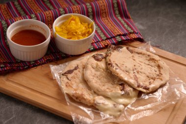 Köy ahşap bir yüzey üzerinde el yazısı ve sos ile servis edilen peynirle dolu pupusalar, canlı bir Salvador mendiliyle tamamlanmış..