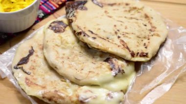 Salvador mutfağı geleneğini vurgulayan, ahşap bir yüzey üzerinde el yazısı ve sos olan peynir dolu pupusaları gösteren pürüzsüz bir video tavası..