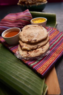 Geleneksel Orta Amerika lezzetlerini vurgulayarak ahşap bir yüzey üzerinde tamale yaprağı üzerinde servis edilen el yazısı ve soslu köpek yavruları..