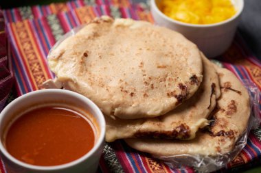 Pupusas with curtido and sauce served on a tamale leaf atop a wooden surface, highlighting traditional Central American flavors. clipart