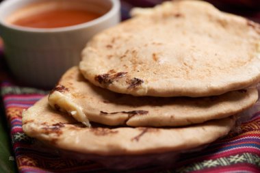 Pupusas with curtido and sauce served on a tamale leaf atop a wooden surface, highlighting traditional Central American flavors. clipart