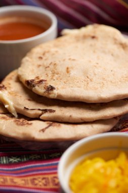 Geleneksel Orta Amerika lezzetlerini vurgulayarak ahşap bir yüzey üzerinde tamale yaprağı üzerinde servis edilen el yazısı ve soslu köpek yavruları..