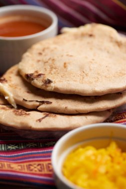 Geleneksel Orta Amerika lezzetlerini vurgulayarak ahşap bir yüzey üzerinde tamale yaprağı üzerinde servis edilen el yazısı ve soslu köpek yavruları..